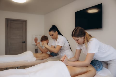 Women receiving back massages from masseuses, practicing relaxation and wellness techniques during a professional training session